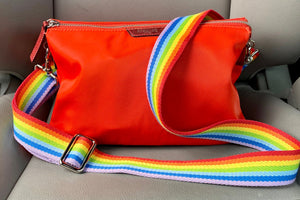Photo of orange purse with colorful rainbow strap attached to it.